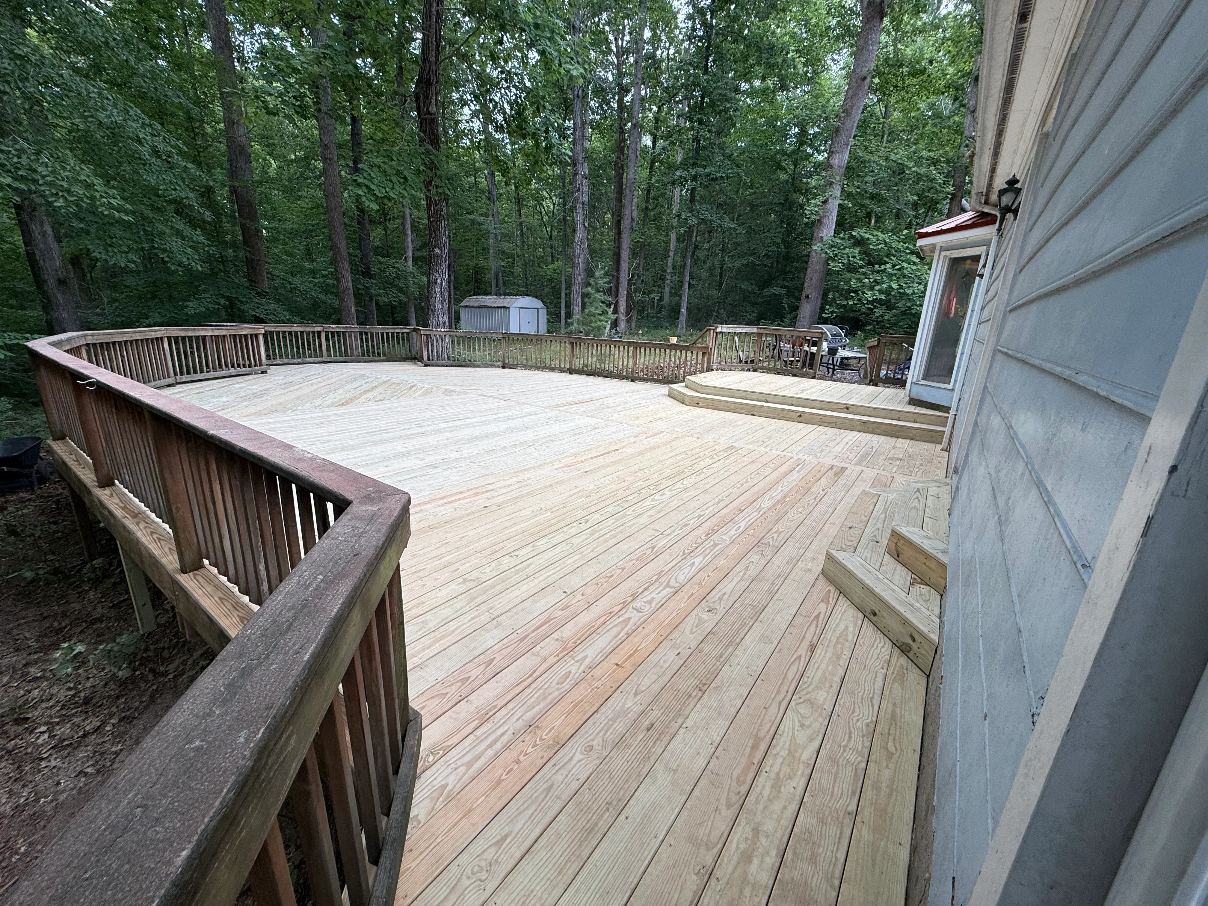 Large composite deck with curved railings, multi-level design, and wooden stairs in wooded setting