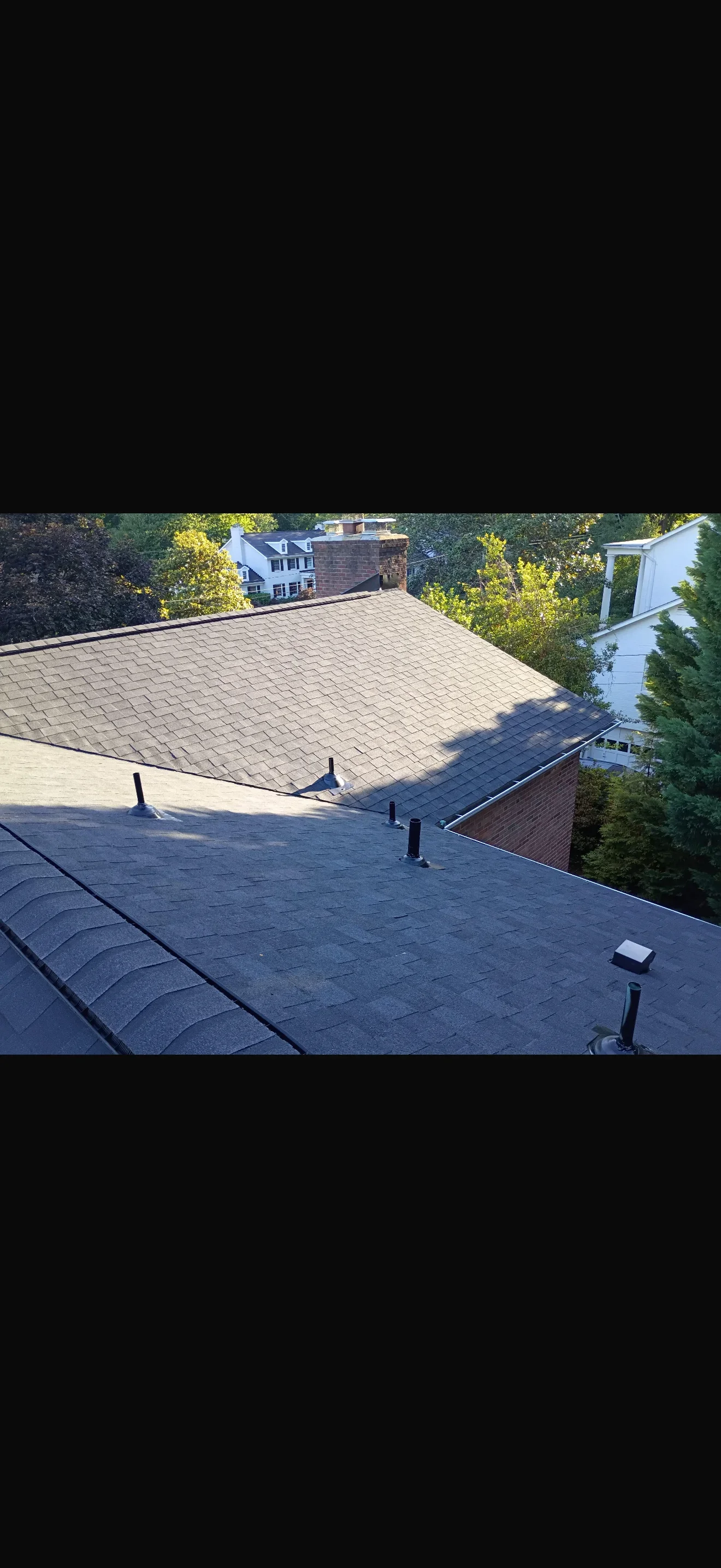Newly installed asphalt shingle roof with tan and dark gray tones, multiple planes, and brick chimney flashing