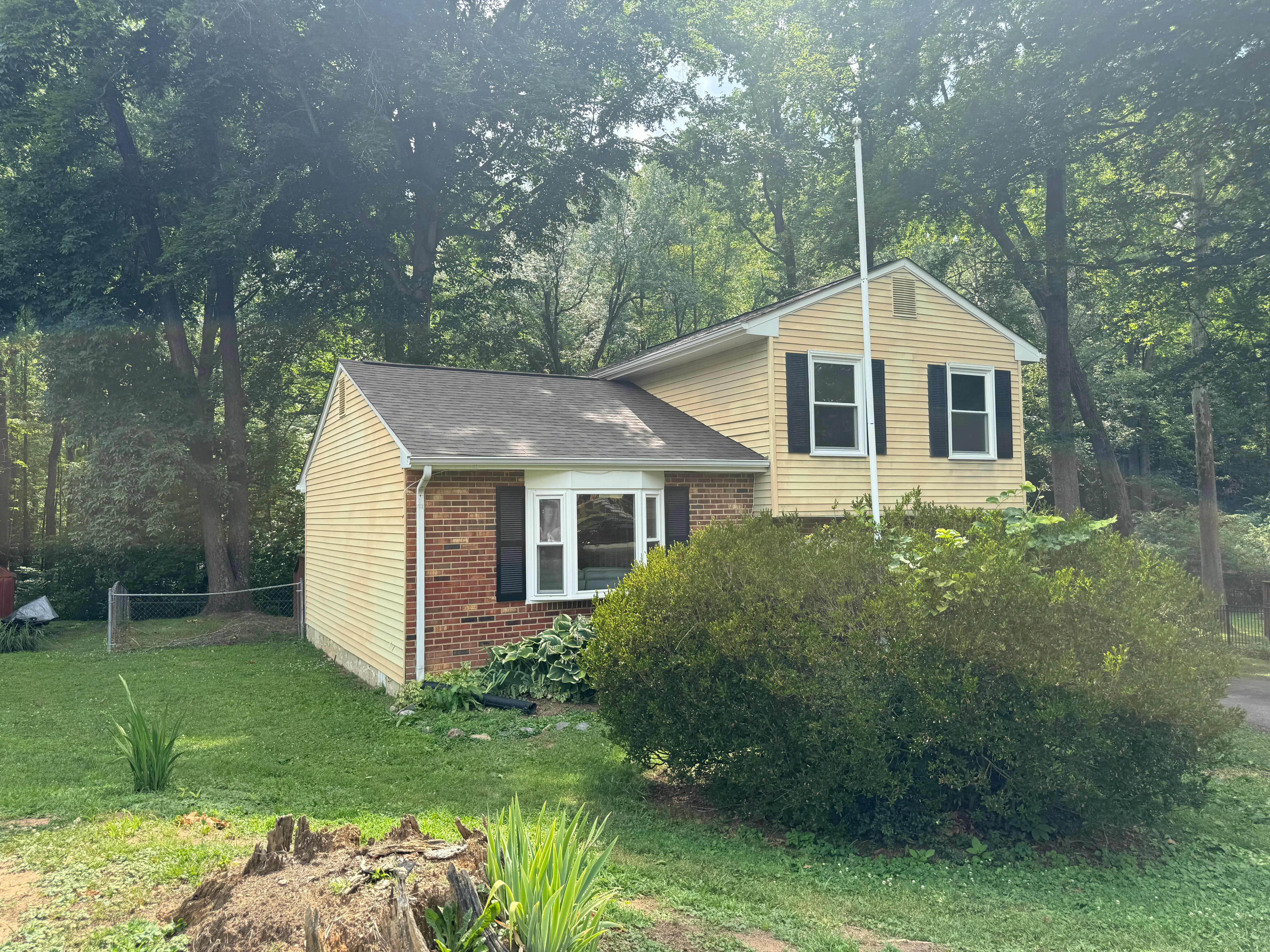 Two-story home with new gray asphalt shingles and cream vinyl siding among mature trees