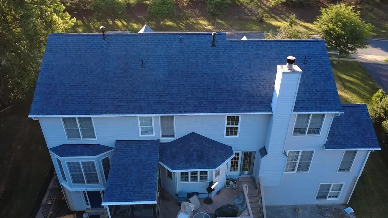 Aerial view of blue architectural shingle roof on white two-story home with multiple peaks and dormers