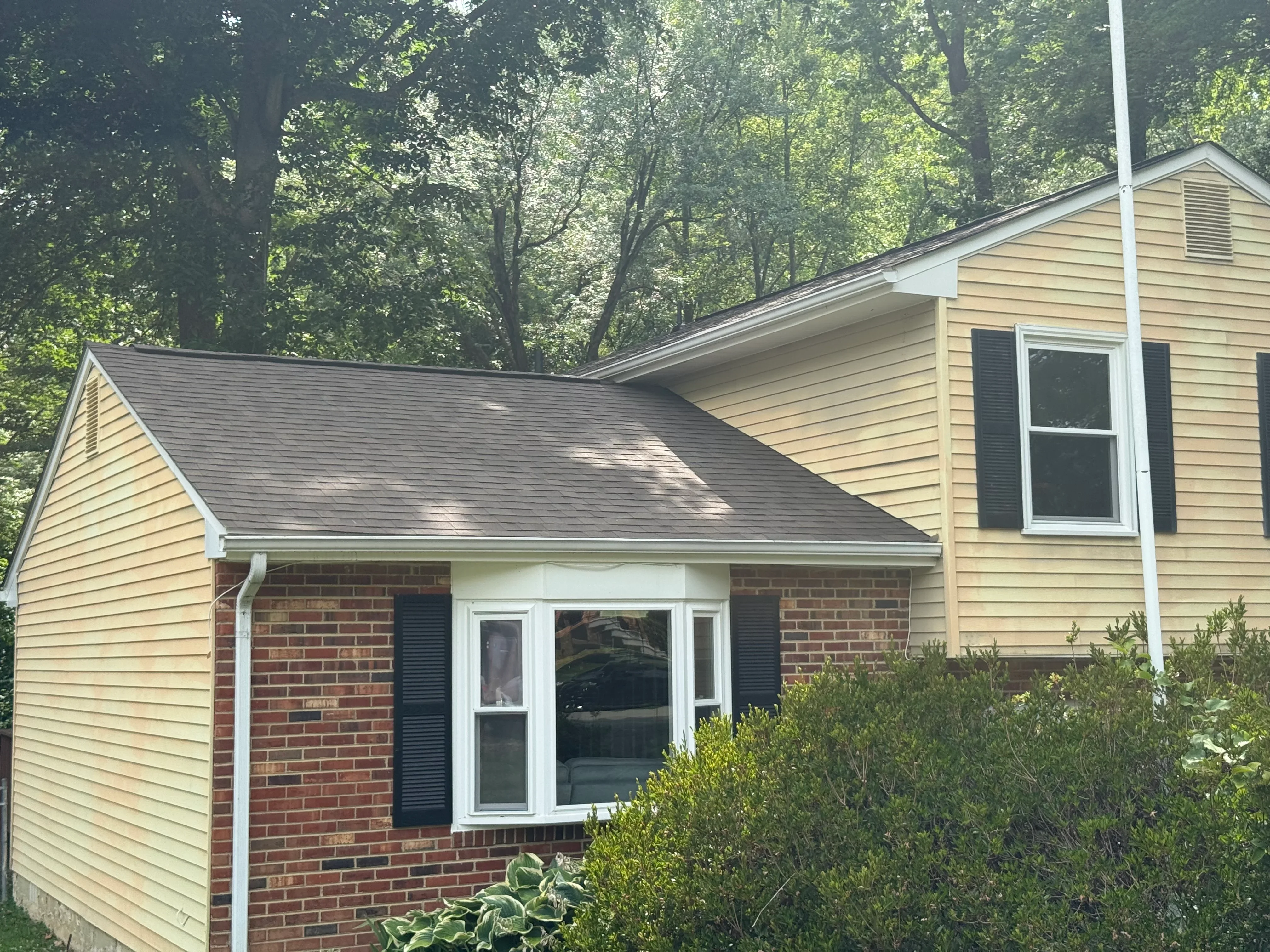 Charcoal gray asphalt shingle roof on brick and siding home with white trim and gutters