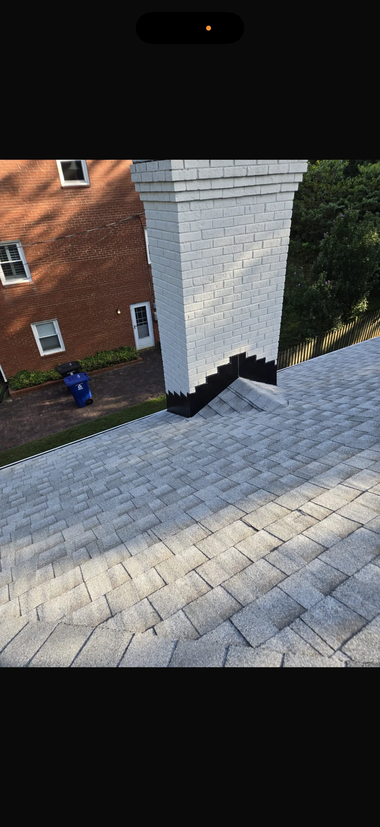 White brick chimney with black waterproofing membrane and gray-tan paver patio in running bond pattern