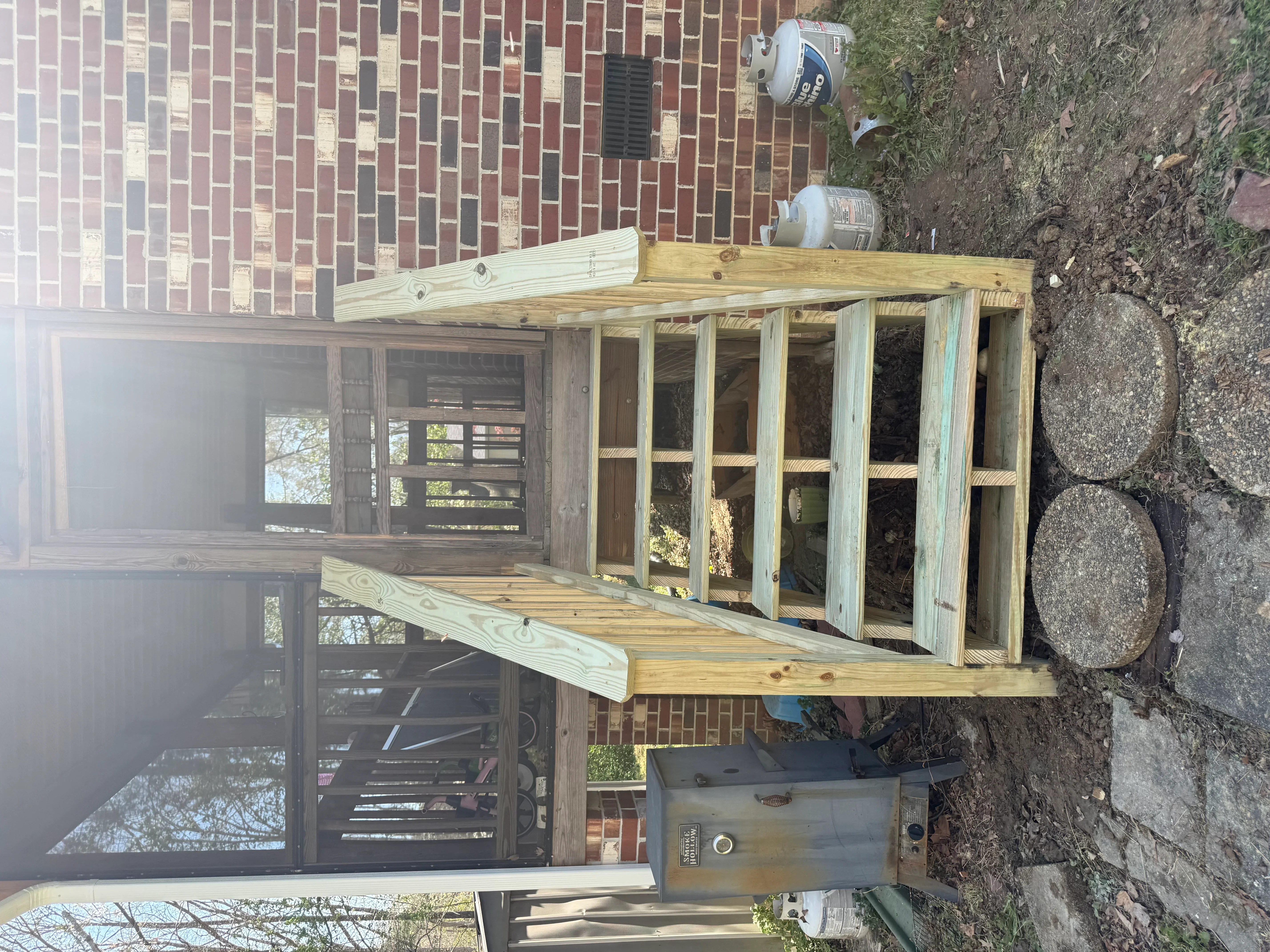 Pressure-treated wood deck with screened room addition and roof framing against brick home